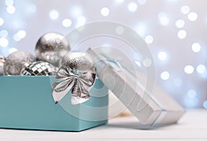 Blue and silver box with silver Christmas balls on the background of blue bokeh lights New Year card