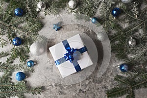 Blue and silver Christmas baubles and a gift on a soft feathery surface in front of defocused blue and white lights