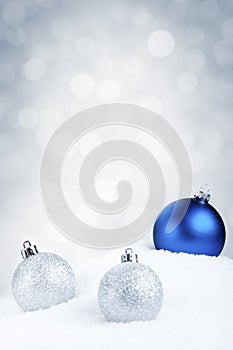 Blue and silver Christmas baubles on snow, silver background