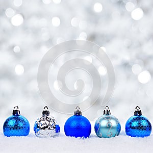 Blue and silver Christmas ornaments in snow with twinkling background