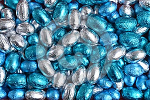 Blue, silver and turquoise foil wrapped chocolate easter eggs, against a black background.