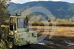 A blue sky above Alp mountains covered with morning mist and an old yellow tractor on the field in a moorland in a cozy village