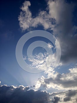 Blue sky background with the sun and rays behind the clouds. Sky heaven in portrait composition.