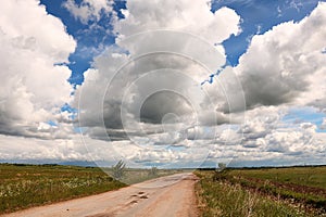 Blue sky background with thunderclouds and country road. Blue, white pastel paradise, soft focus lenses, glare of sunlight.