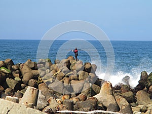 blue sky, blue sea and fishermen walking on the rocks breaking the waves. White splashes of broken waves