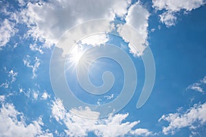 blue sky with bright sun and rays, white cumulus clouds around