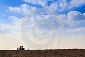 blue sky clouds above dark ploughed field seeder in spring