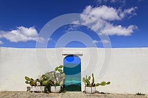 Blue sky with clouds, blue door with prickly pear and the traditional white wall in the town of Ostuni in Apulia, Italy.