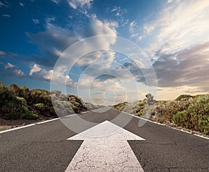 Blue sky with clouds and country road with white arrow