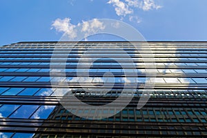 The blue sky with clouds and modern office building is reflected in the glass of Windows of a skyscraper