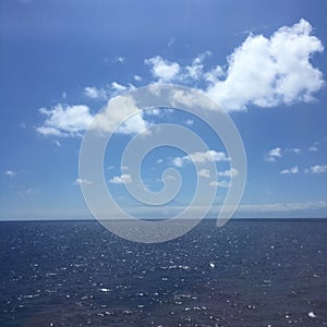 Blue sky with clouds in the ocean with an island on the horizon