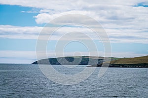 Blue sky with clouds over the hilly coast of Ireland. Seaside landscape on a sunny day. Body of water near mountains under white