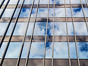 The blue sky with clouds is reflected in the glass of identical windows of modern office building