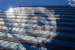 The blue sky with clouds is reflected in the glass of identical windows of modern office building