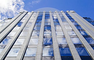 The blue sky with clouds is reflected in the glass of identical windows of modern office building