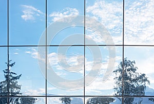 Blue sky, clouds and trees reflection in grid of glass window of modern office building. Nature vs business structures