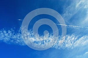 Blue sky crossed by contrail and scattered clouds