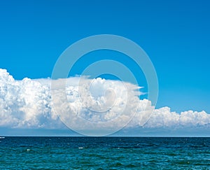 Blue sky with cumulus clouds over sea. Colorful seascape with horizon line and calm sea water, fine ripples.