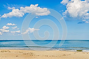 Blue sky with fluffy clouds, over clear sea water, beach with g