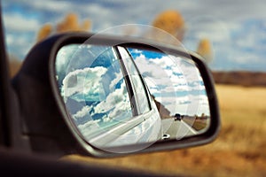 Blue sky with fluffy clouds and road reflection an car mirror