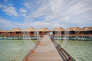 Blue sky horizontal picturesque wooden bridge walkway leading to a Row of Luxury Overwater Villa at a resort island, Maldives