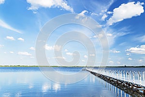 Blue sky with light clouds, water, white pier in the summer day.