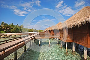 Blue sky luxury overwater with wooden platform walkway at a secluded tropical resort island, Maldives