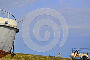 Blue sky. Old rusty abandoned boats, white ships lie on green grassy shore in the light of setting sun. Man. Lake Baikal