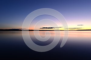 Blue sky in the orange twilight glow on horizon over calm azure water lake