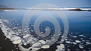 Blue sky reflected in the water of the waves on the sand.