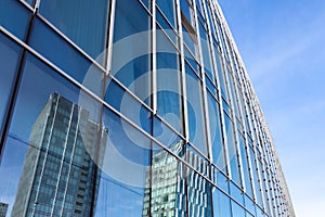 The blue sky is reflected in the windows of a modern office building. Architecture and exterior of contemporary houses