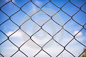 Blue sky through rusty wire mesh fence. Blur background, texture. Close up view, wallpaper