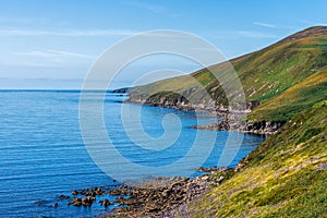 Blue sky and sea with rocky coastal line and green hills