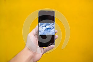 Blue sky on smartphone display and yellow background