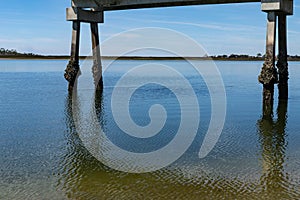 Blue sky and still water reflection with pier pilings encrusted with oysters and barnacles, Tybee Island Georgia