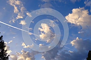 Blue sky, sunny clouds and the white airplane contrail trail, background.