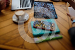 Blue sky and trees reflection in smartphone and tablet on unfocused wooden cafe table. Unfocused cappuccino cup, laptop on