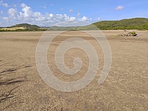 Panoramic photo of dry salt pans of ocher color. Blue sky with tropical clouds and mountains with vegetation. Martinique, French