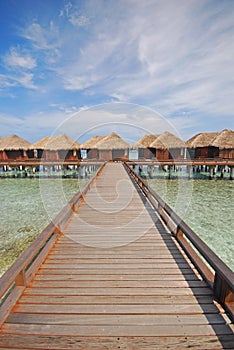 Blue sky turquoise water wooden bridge walkway leading to a Row of Overwater Villa at a resort island, Maldives