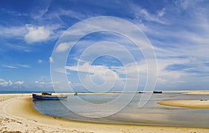 Blue sky, white clouds, boat on a sandbank, sea