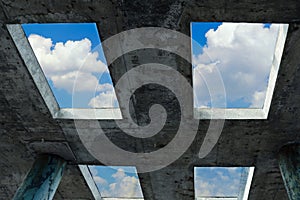 A blue sky with white clouds can be seen through the windows in a concrete building. The concept of faith, freedom and hope.