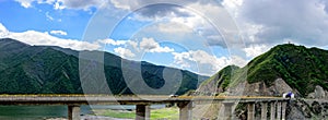 The blue sky, white clouds, green mountains and lake water, the cars driving out of the tunnel are speeding on the viaduct