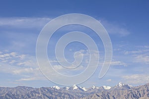 A blue sky with white clouds over the desert mountains with snowy peaks. Daytime in the mountains