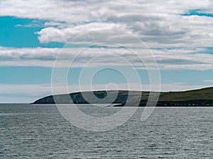 Blue sky with white clouds over the hilly coast of Ireland. Seaside landscape on a sunny day. Body of water near mountains under