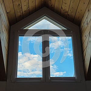 Blue sky and white clouds seen through a large dormer window in a wooden roof