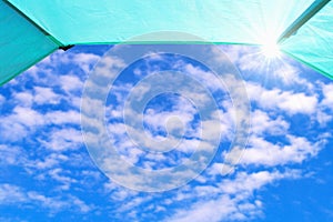 Blue sky with white clouds and sun rays seen from inside a tent.