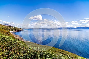 Blue sky with white puffy clouds over rocky coastal line and mountains in a distance