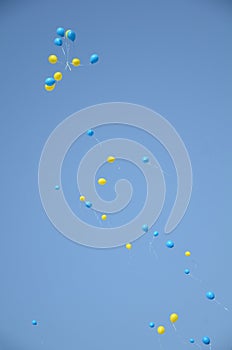 Blue sky, yellow and blue balloons are flying from happy people.