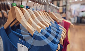 Blue sleeveless shirt on wooden hanger hanging on rack in clothing store for sale. Fashion retail shop inside shopping center.