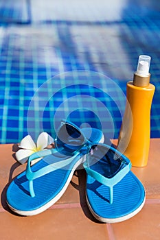 Blue slippers with sunscreen cream and sunglasses on border of a